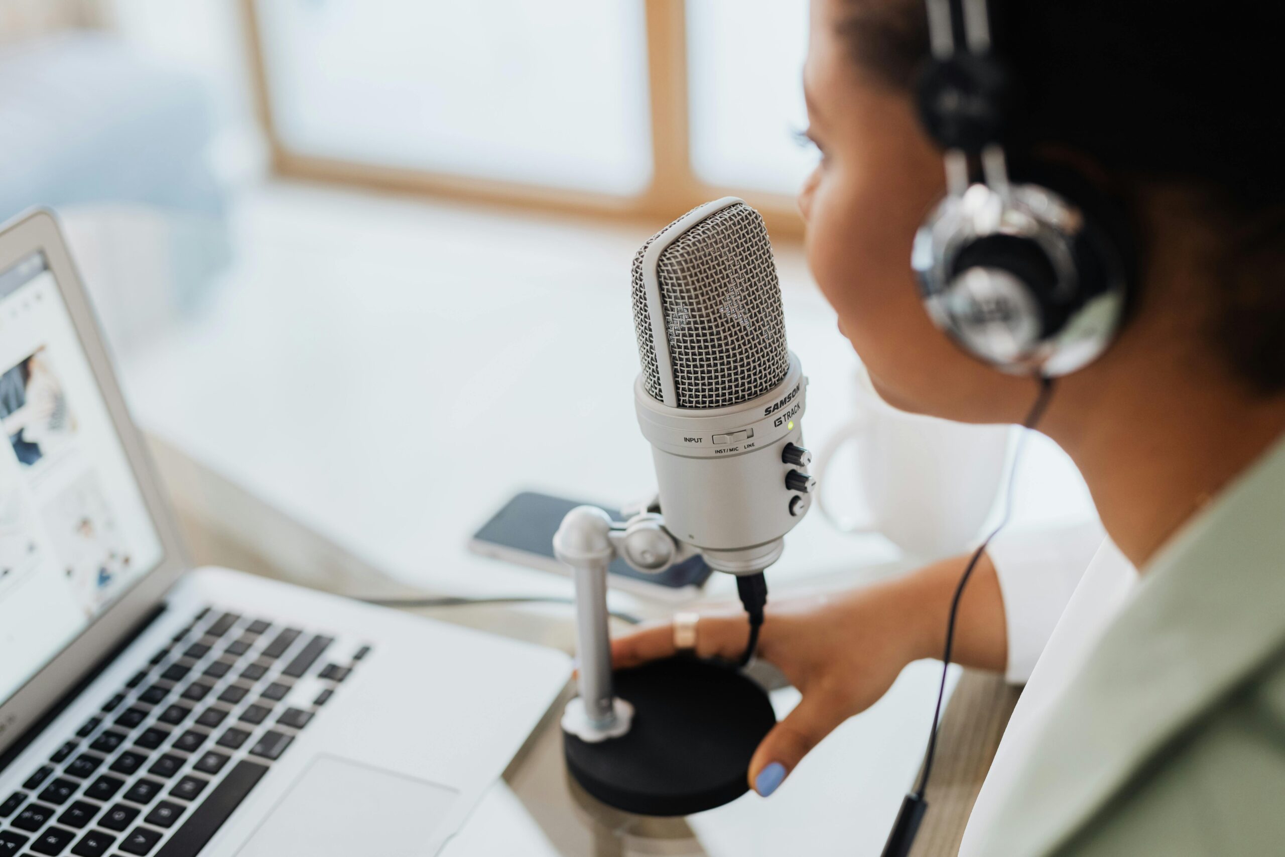 Side profile of a woman sitting in front of a laptop while wearing headphones and speaking into a microphone